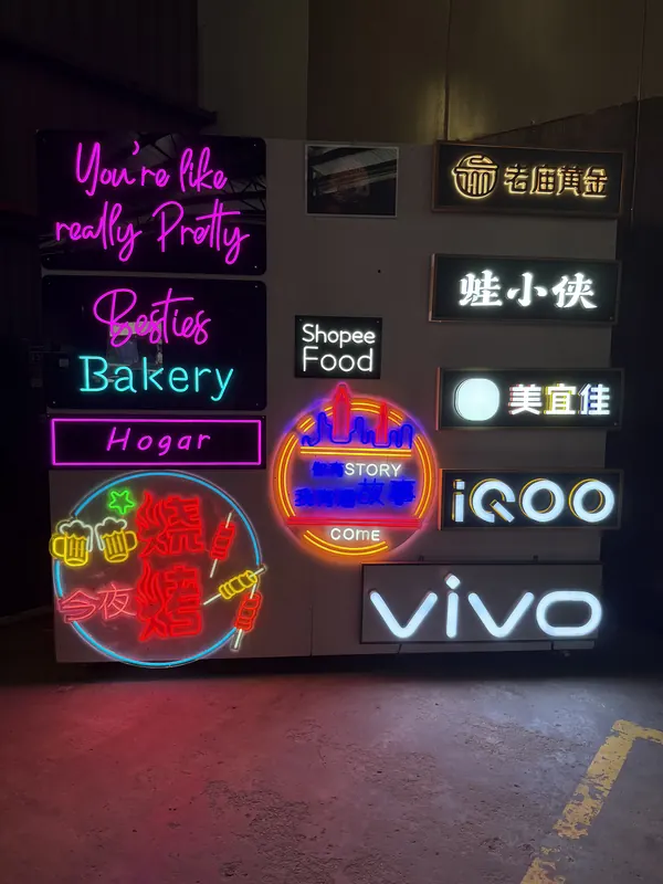 The same wall switched on: LED neon script, a neon outline badge and frontlit letters.